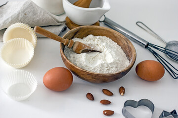 Homemade baking ingredients and accessories. A jar of sugar, a cup of flour, eggs, a whisk, a cake pan, a napkin, nuts on a white table. Home hobbies authentic cooking concept, close-up, copy space