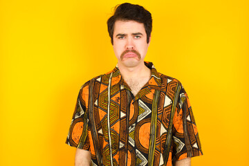 young Caucasian man wearing printed shirt against yellow wall crying desperate and depressed with tears on his eyes suffering pain and depression. Sad facial expression and emotion concept.