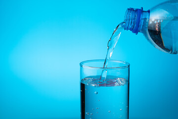 A glass filled with water from a plastic bottle on a blue background. Side view with copy space.