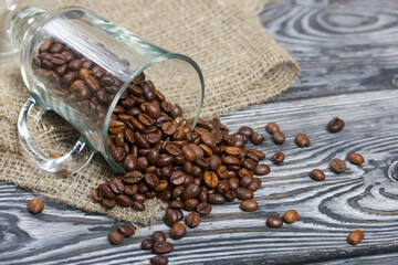 Overturned glass cup with coffee beans. The coffee beans scattered on linen and pine boards. Close-up shot.