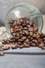 Overturned glass cup with coffee beans. The coffee beans scattered on linen and pine boards. Close-up shot.
