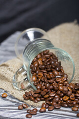 Overturned glass cup with coffee beans. The coffee beans scattered on linen and pine boards. Close-up shot.