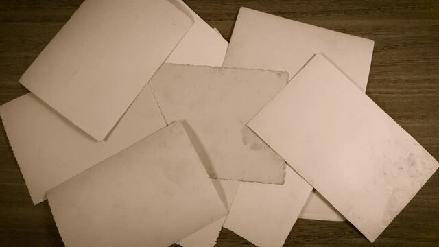 Closeup top view of stack of old vintage paper photos appear stacked together on brown wooden table surface background. Back view of photo pictures