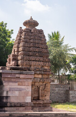 Aihole, Karnataka, India - November 7, 2013: Chakra Gudi temple. Brown stone Vimanam tower on top of inner sanctum under light blue sky with plenty of green foliage.