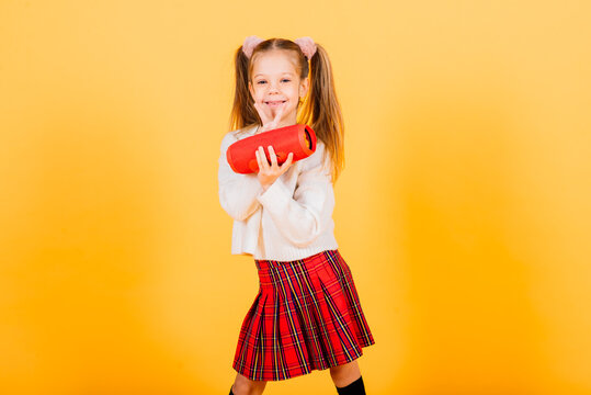 Young cute girl smiling and dancing with wireless portable speaker on yellow studio background.