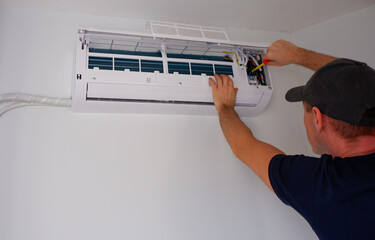 Maintenance of the air conditioner. The service engineer unscrews the contacts with a screwdriver. View of the hands.