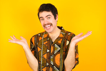 So what? Portrait of arrogant young Caucasian man wearing printed shirt against yellow wall...
