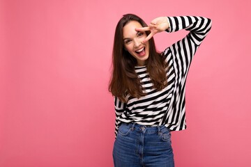 Photo of young european positive smiling winsome happy beautiful brunette woman with sincere emotions wearing casual striped pullover isolated on pink background with copy space