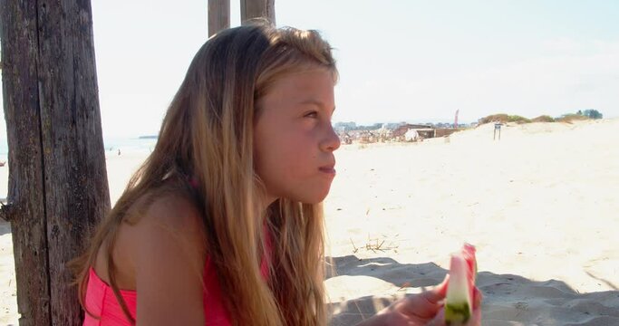 Smiling 9 years old girl eating watermelon on the beach. Child eating tasty summer fruit. Happy summertime. 4k slow motion