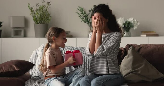 Little daughter congratulates mom gives her gift box. Mommy cover eyes with hands in anticipation receive surprise from small kid. Family celebrate life event, Mother Day expressing love care concept