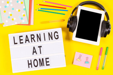 Learning at home. Digital tablet computer with headphones, lightbox, school supplies on yellow background. Top view