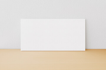 Rectangular blank canvas of 2x1 proportions on light wooden surface and white wall to present artwork, illustrations or photos. 3D Rendering