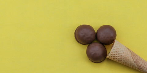 Chocolate ice cream on yellow.
Chocolate ice cream in a cone on the right against a yellow background with space for text on the left, top view close-up.