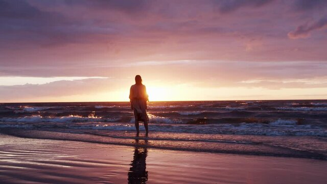 Silhouette of a woman standing in serenity on a beach and looking into dusk sunset over the sea.