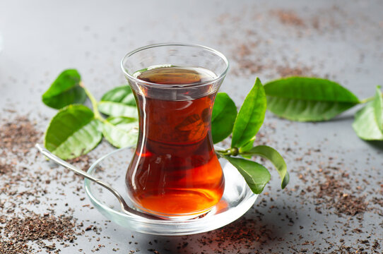 Glass cup of black tea with fresh tea leaves, traditional turkish brewed hot drink
