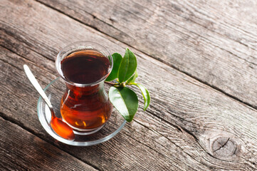 Glass cup of black tea with fresh tea leaves on wooden background, traditional turkish brewed hot drink