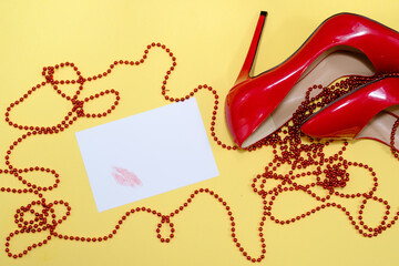 female shiny red stilettos and a card with a lipstick print  on a yellow background