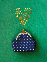 Glitter confetti golden heart from polka dot purse on green background