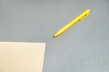 Flat lay of yellow pen lying near a designer paper on a gray surface