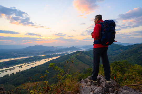 Senior man enjoys the view of cliff after hiked the hill to watch the sunrise over mekong river in morning at phu pha dak in nong khai, Thailand