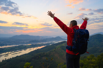 Senior man standing the cliff open arms enjoying the view of Mekong river at sunrise at phu pha dak in nong khai, Thailand