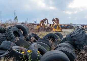 Industrial graveyard with discarded large tires and heavy equipment attachments along the river