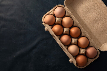 brown chicken eggs in an open egg carton isolated on black table. Fresh chicken eggs background. Top view with copy space. Natural healthy food and organic farming concept. Eggs in container