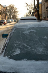 All the windows of the parked cars are covered with snow and ice. Frost on the windshield in the...