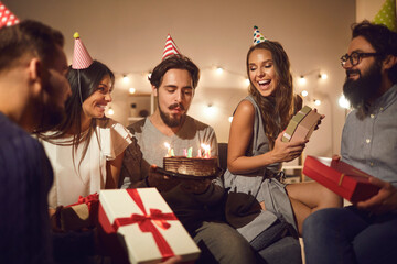 Young birthday man makes a wish and blows out the candles on the cake surrounded by his friends.