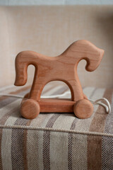 Fototapeta na wymiar Wooden horse on wheels, children's toy on a sofa.