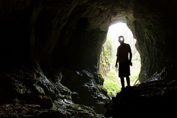 Tourist in the Occidental Carpathians, Radesei Cave, Romania. Entrance to the cave, the silhouette...