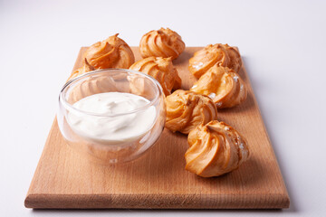 Custard cup and choux pastry profiteroles on a wooden board on a white background.