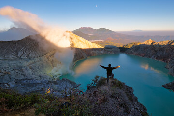 Happy man standing on the cliff raise hand enjoying of Kawah Ijen crater in east java, Indonesia
