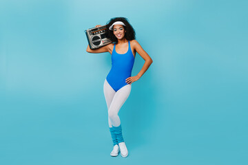 Winsome african girl in aerobics form enjoying training. Studio shot of attractive black lady with boombox looking at camera.