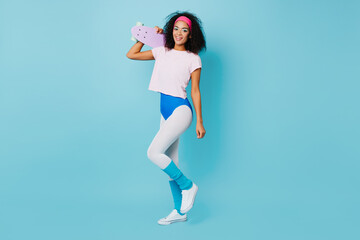 Full length view of blissful african lady with skateboard. Studio shot of joyful curly girl in aerobics form.