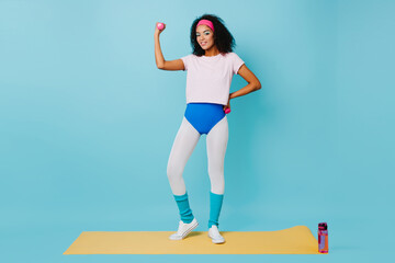 Joyful african woman training with dumbbells. Studio shot of fit adorable girl in aerobics form.