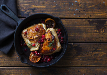 Fried chicken thighs with lemon and cranberries in a skillet on wooden table