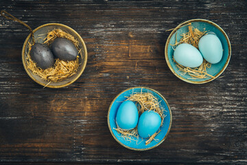 Three small colorful bowls filled with Easter eggs in the same color on rustic wood, Easter decoration, shabby style, top view with copy space