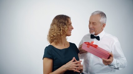 A loving old husband gives a gift box to a joyous attractive mature wife.