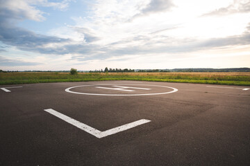 Fototapeta premium A large area with a special symbol in the center for helicopter landing. Private helipad in a green field against the backdrop of evening clouds.