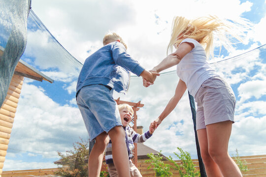 Mom with children jumping together and having fun on a trampoline on a green lawn.
