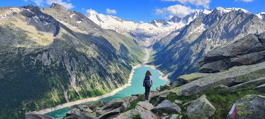 A girl hiking towards the Olperer hut with amazing views of Alpine lake Schlegeis in the valley...