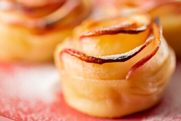 Closeup of rose bud with apples. Apple pie sprinkled with powdered sugar on a pink surface. Shallow depth of field.