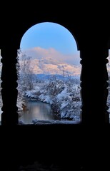 View of snowy landscape through window of an old wooden bridge