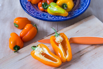 High angle selective focus view of orange mini bell pepper open in half on wooden cutting board,...