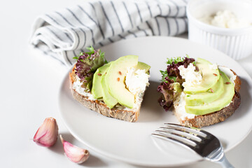 Two toasts with cottage cheese, lettuce and avocado slices are on a gray plate. Healthy food theme. Free space for text.