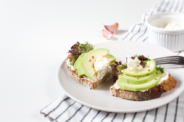 Two toasts with cottage cheese, lettuce and avocado slices are on a gray plate. Healthy food theme. Copy space.