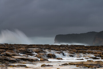 Rock platform, cascades and splashes with rain clouds by the seaside