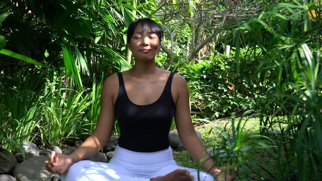 Balinese female meditating in lotus pose searching calm mindfulness for recreating and feeling vitality, woman in sportive clothes practice hatha yoga in nature environment for get energy
