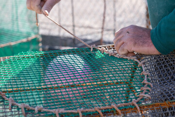 Close-up of the hands of an elderly fisherman in the harbor dock as he repairs fishing nets using...